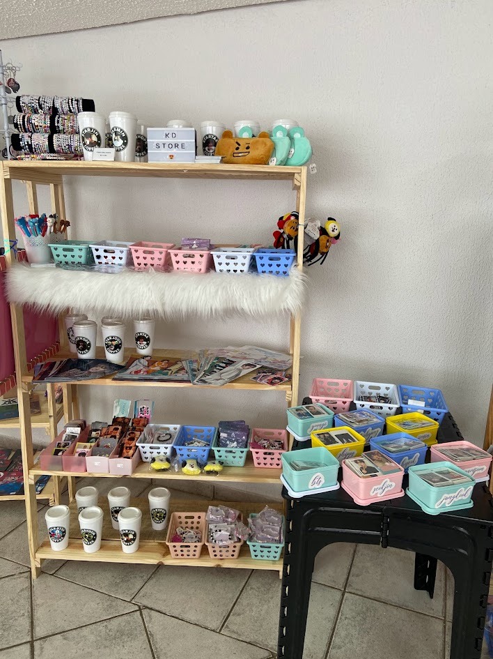 Primeiro estande da KD Store em evento de K-pop mostrando produtos fanmade artesanais no in&iacute;cio da loja